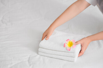Female hands with clean towels and pink plumeria flower on bed in hotel room, closeup