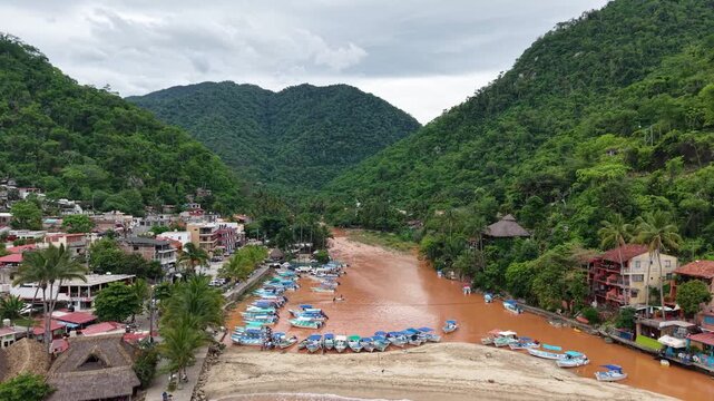 Zoom in desde un dron sobre el rio de Boca de Tomatl&aacute;n pueblo ubicado al sur de puerto vallarta, Jalisco. rio color marron por las lluvias, peque&ntilde;os barcos azules, monta&ntilde;as selvaticas verdes, nublado