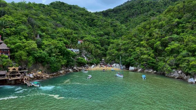 Zoom in de toma aerea con dron de la playa colomitos la mas peque&ntilde;a de M&eacute;xico, rodeada de monta&ntilde;as selvaticas, peque&ntilde;os botes llegando a la playa y personas tomando el sol