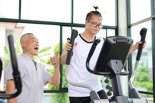 A man with down syndrome exercising on an elliptical machine under the guidance of an elderly man at the gym
