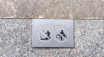 Sign aluminum No fishing or climbing on ground square concrete floor of sidewalk.  Warning of prohibited areas playing various devices. Regulations must be followed installed along river and fence
