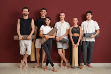 Fototapeta premium Group of sporty young people with yoga mats near red wall