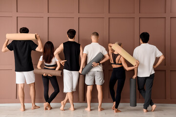 Fototapeta premium Group of sporty young people with yoga mats near brown wall, back view