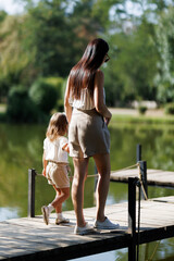 Mother and daughter enjoying a serene stroll on a peaceful lakeside boardwalk surrounded by lush...
