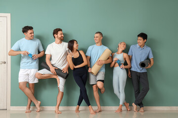 Fototapeta premium Group of sporty young people with yoga mats and water bottles near green wall