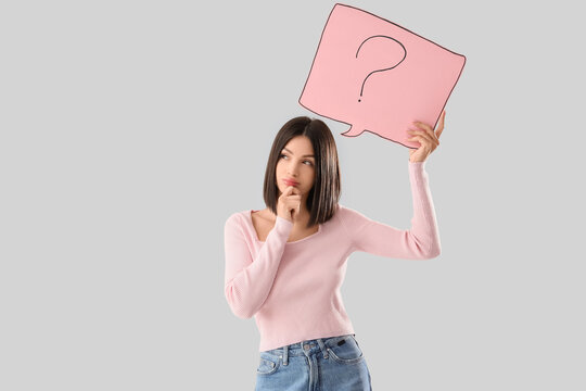 Fototapeta Thoughtful young woman holding speech bubble with question mark on light background
