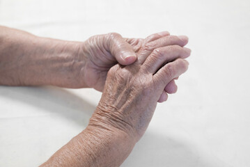 Fototapeta premium Two hands of an elderly person. The skin of the hands is thin, with pronounced wrinkles and veins, which indicates age. One hand holds the other. The color scheme of the photo is neutral, with light s