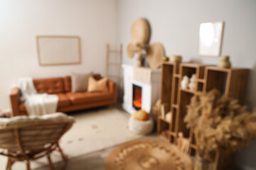 Interior of living room with leather sofa, armchair, shelving unit, ladder, fireplace and autumn decorations, blurred view