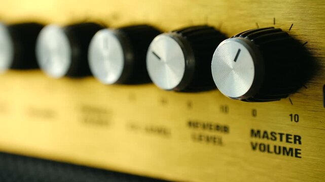 Close up musician hand turning up master volume knob on vintage style golden guitar amplifier, increasing sound level for powerful music performance or rehearsal. Turning up volume guitar amplifier