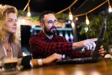 Collaborative team working on a laptop in a modern cafe environment with string lights, discussing ideas with focus and determination