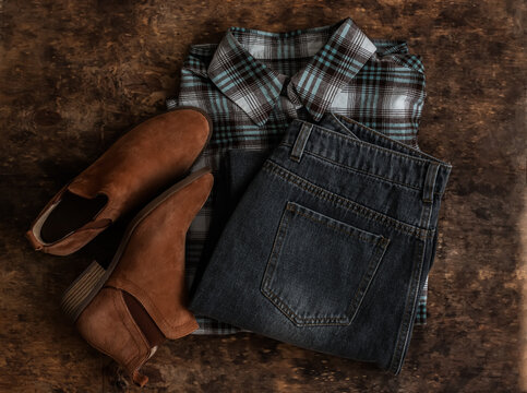 Grey jeans, plaid cotton shirt, chelsea suede boots on a wooden background, top view
