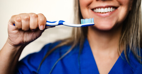 Female dentist smiling with toothbrush in clinic uniform closeup