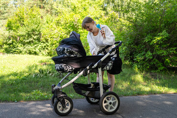 Fototapeta premium Happy young mother showing baby rattle to her newborn baby, walking outdoors in park.