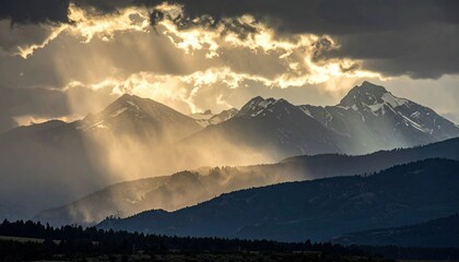 Sun Rays Shining Through Clouds Over Mountain Range With Snow Capped Peaks in Dramatic Golden Hour Light