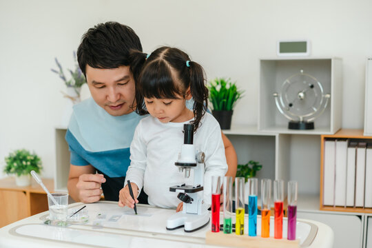toddler girl scientist using tongs putting small herbal sample in slide with father, preparing specimen for science microscope