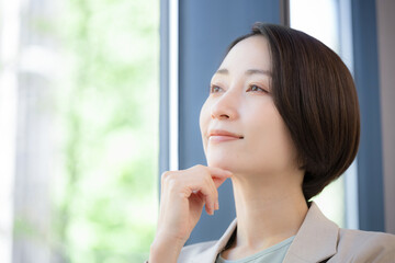 窓際で考えるビジネスマンの女性　キャリアに悩む転職どうしようかな