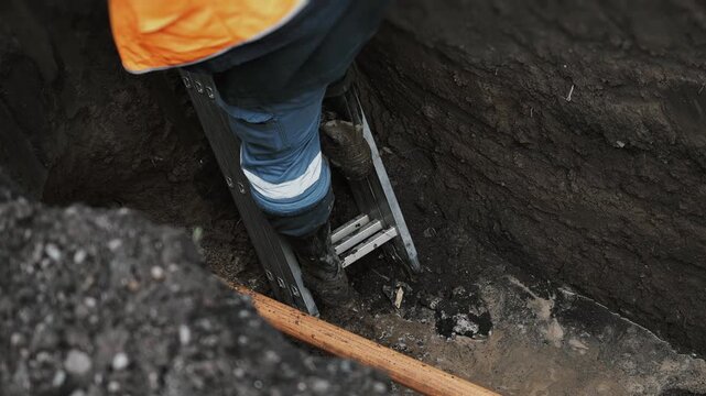 A drilling rig worker descends a ladder into a pit and checks the connection between the drill and the gas pipe. Laying plastic gas pipes underground.