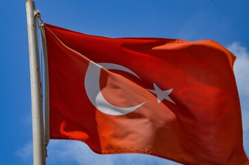The Turkish flag flutters in the wind against a blue sky
