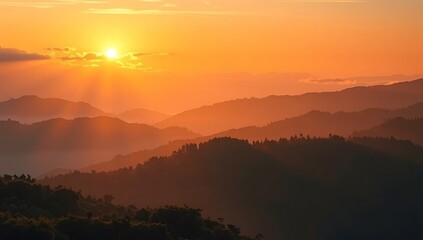 Majestic mountain range silhouetted against a vibrant orange sunset sky with sun rays.