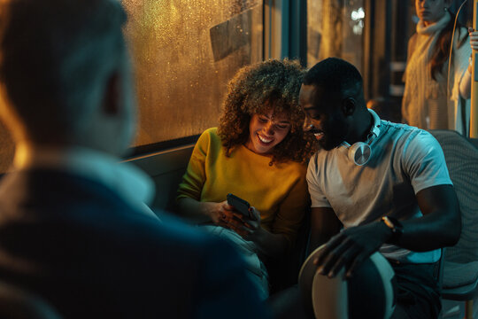 Two young people looking at a smartphone on a bus at night
