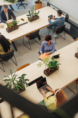 Coworkers using laptops and digital tablets in modern office with plants