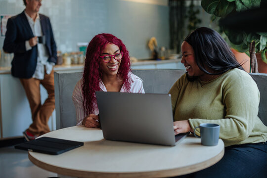 Two happy businesswomen collaborating on laptop in modern office