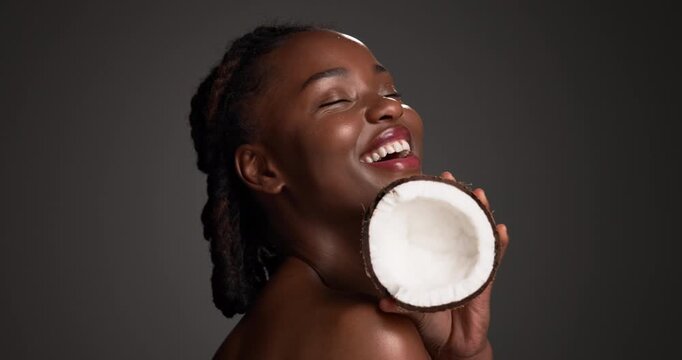 Coconut, skincare and smile with face of black woman in studio for beauty, organic cosmetics or oil treatment. Self care, dermatology and glow with person and fruit on dark background for moisturizer