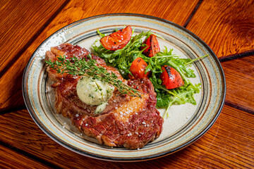 A perfectly cooked steak topped with herb butter alongside vibrant grilled tomatoes and arugula