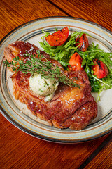 A succulent steak topped with herb butter is served with vibrant salad on a wooden table