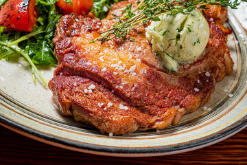 Savory and perfectly cooked steak topped with herb butter, accompanied by fresh greens and tomatoes