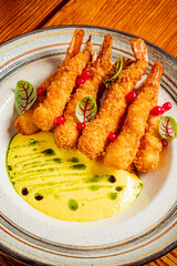 A plate of crispy shrimp is beautifully arranged with a bright green sauce and garnishes