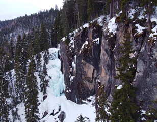 Frozen waterfall on a snowy cliff in a forest