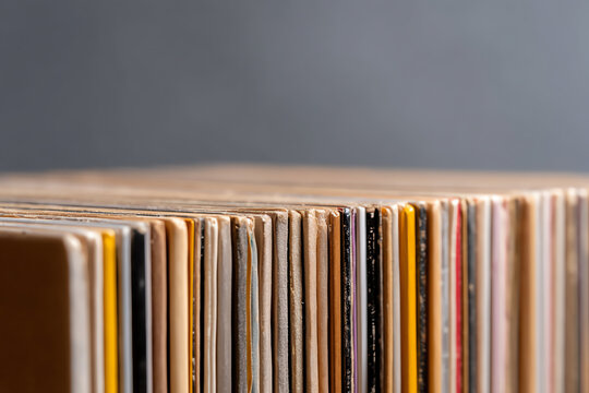 Close-up of a row of vinyl record covers arranged vertically, showcasing their worn edges and varied colors against a neutral background
