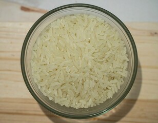 Uncooked rice in a glass bowl on a light-colored wooden surface