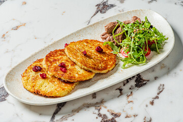 Deliciously crispy potato pancakes served alongside bright green salad and tender meat slices