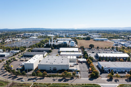 Aerial drone picture of a large business and office park in Hillsboro Oregon, showing multiple commercial buildings, tree lined streets, and parking lots surrounded by suburban environment in fall 