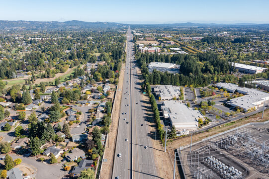 Aerial drone picture of traffic on US 26 highway in Hillsboro Oregon during a clear fall day, showing multiple lanes of cars and trucks moving under blue sky with surrounding suburban and rural are