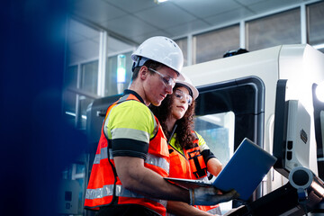 Two workers in orange vests are looking at a piece of machinery