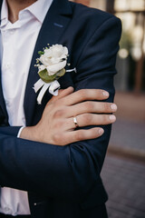 The groom on his wedding day, dressed in a classic suit, shows off a gold wedding ring on his finger and a boutonniere of fresh flowers attached to his jacket