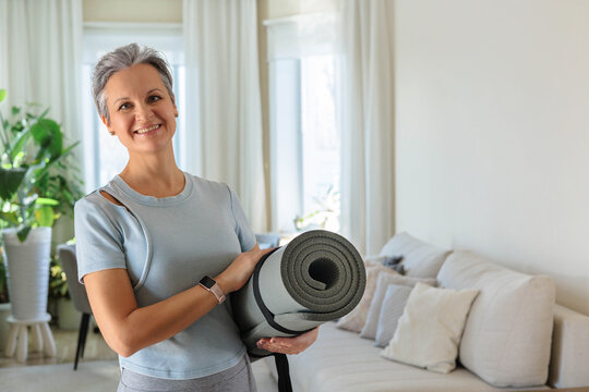 An elderly smiling yogi woman with gray hair is going to practice at home. A mature woman. 