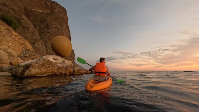 Kayaking, sunset, ocean, man paddles kayak along a scenic rocky coastline during golden hour, tranquil waters