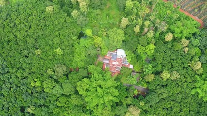 Top-down aerial view of a large, secluded traditional house with solar panels, completely surrounded by a dense tropical jungle in Kerala, India, representing a hidden eco-retreat or off-grid living.
