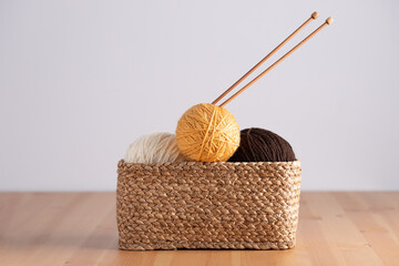 Wicker basket with yarn balls and knitting needles on wooden table, horizontal frame with negative...