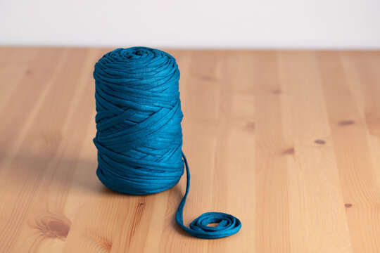 Teal blue yarn spool on light wooden table. Horizontal minimalist image with neutral background and copy space. Concept of handmade crafts and DIY lifestyle