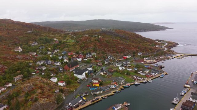 A stunning aerial shot of Petty Harbour Newfoundland in autumn featuring colorful houses winding roads and tranquil harbour waters set against rolling hills under crisp fall skies.
