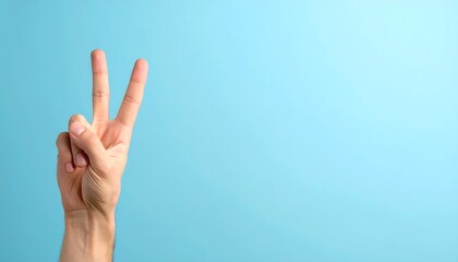 Fototapeta premium Male hand showing two fingers up greeting gesture on blue background. Peace or victory sign concept for communication and positivity.