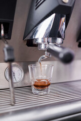 Espresso shot being extracted from a coffee machine into a small glass cup in cafe bar setting.