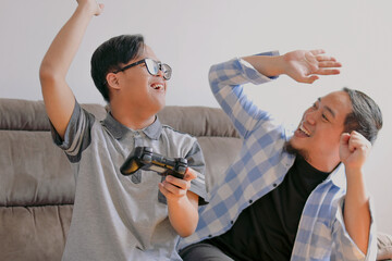 Excited Dad and His Special Needs Boy Celebrating Video Game Victory with Laughter on a Couch