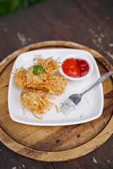 Fried noodle balls served with chili sauce on a white plate. Crispy Indonesian snack made from noodles, perfect for appetizer or street food photography.