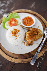 Indonesian fried chicken with steamed rice, sambal chili sauce, and fresh vegetables served on a rustic wooden table. Traditional Asian lunch dish.
